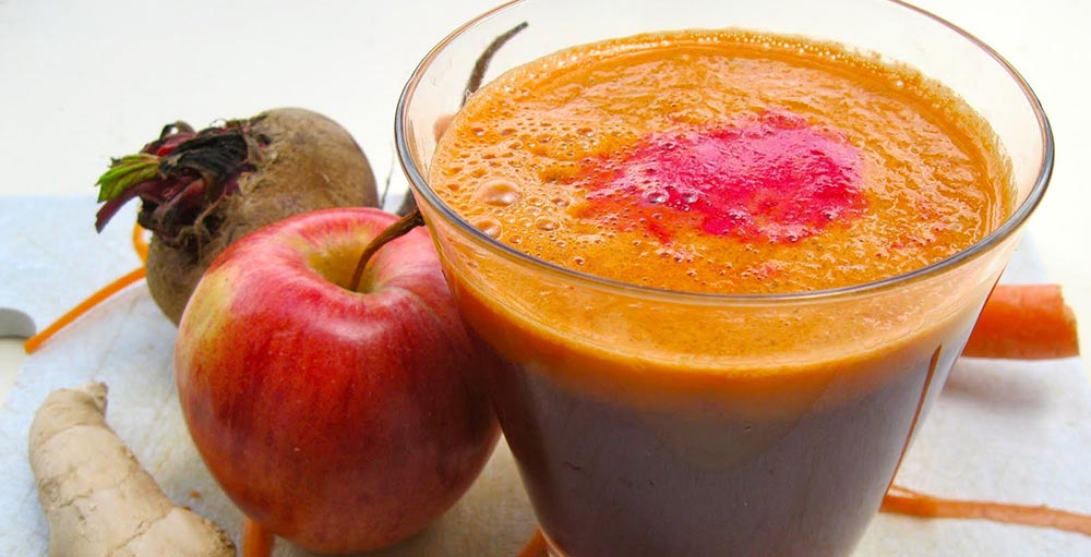 Ecco un bicchiere di succo di frutta con barbabietola, mela rossa e zenzero su una superficie bianca.