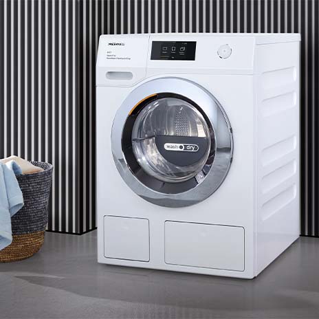 Lavatrice bianca con obl� circolare e cesto di biancheria. Sfondo a righe verticali bianche e nere. Pavimento grigio.