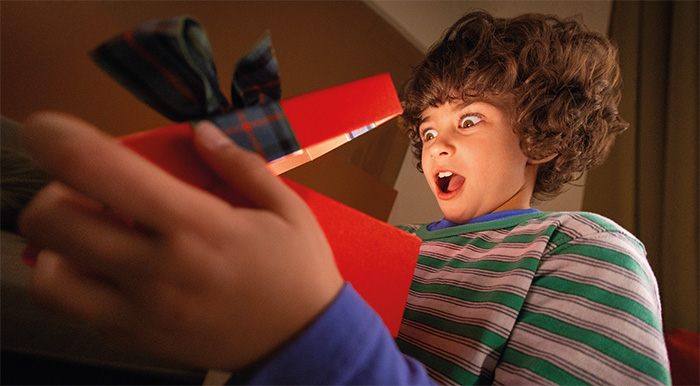 un bambino felicemente sorpreso sta aprendo un regalo di natale in un pacco rosso