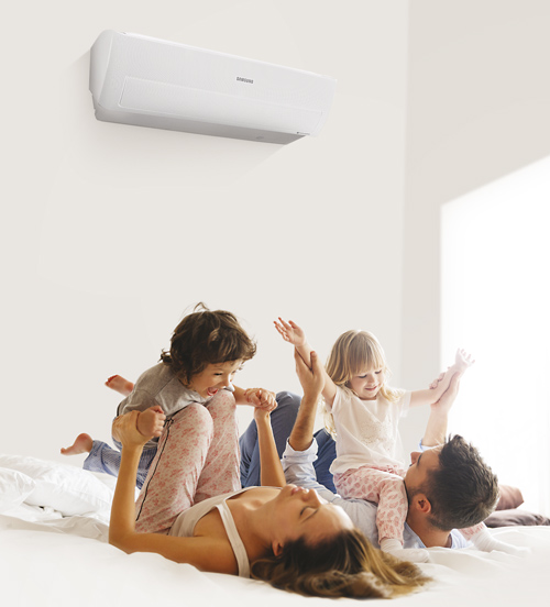 Famiglia di quattro persone sul letto, con condizionatore bianco in alto sulla parete.