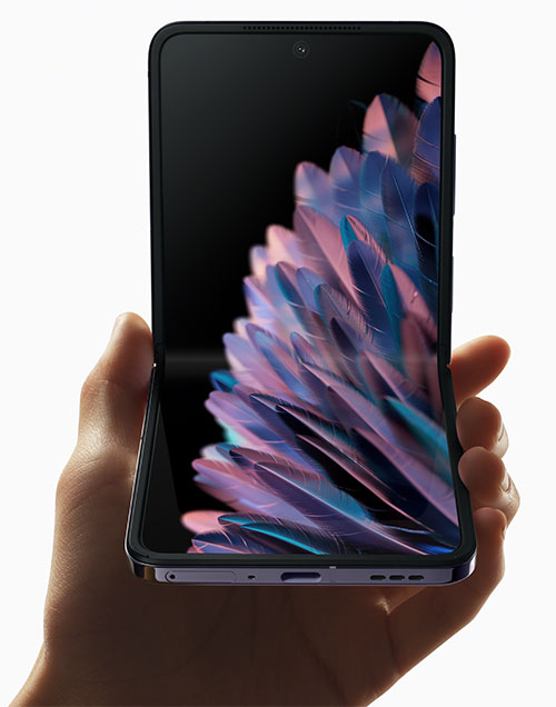 Una mano tiene un telefono pieghevole aperto con uno sfondo di piume blu e rosa.