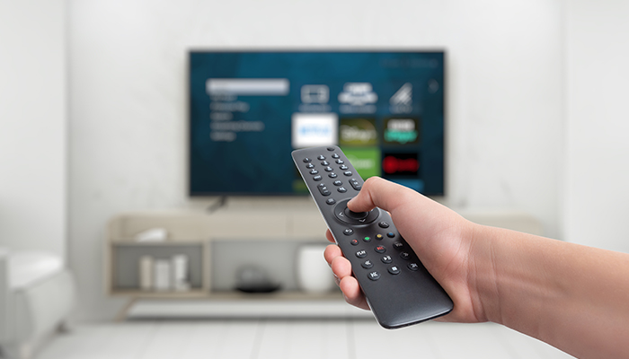 Mano che tiene un telecomando nero con una TV che mostra un menu sullo sfondo.