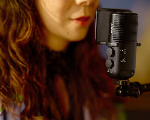 Primo piano di donna con microfono nero Sony. Il microfono � montato su un supporto nero. Sfondo sfocato.