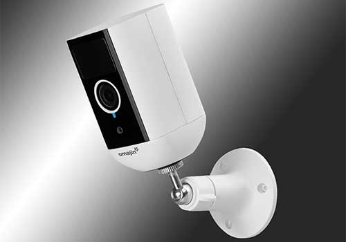 Telecamera di sicurezza bianca con montaggio a parete su sfondo sfumato grigio e bianco.