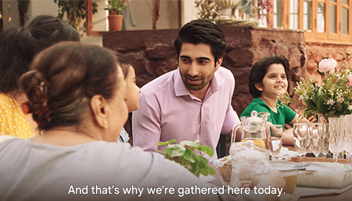 una famiglia al tavolo, mangiano e parlano, in basso ci sono i subtitles (scena di un film indiano)