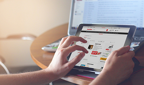 Su un tavolo di legno, mani interagiscono con un tablet che mostra un sito web. Un laptop � visibile sullo sfondo.