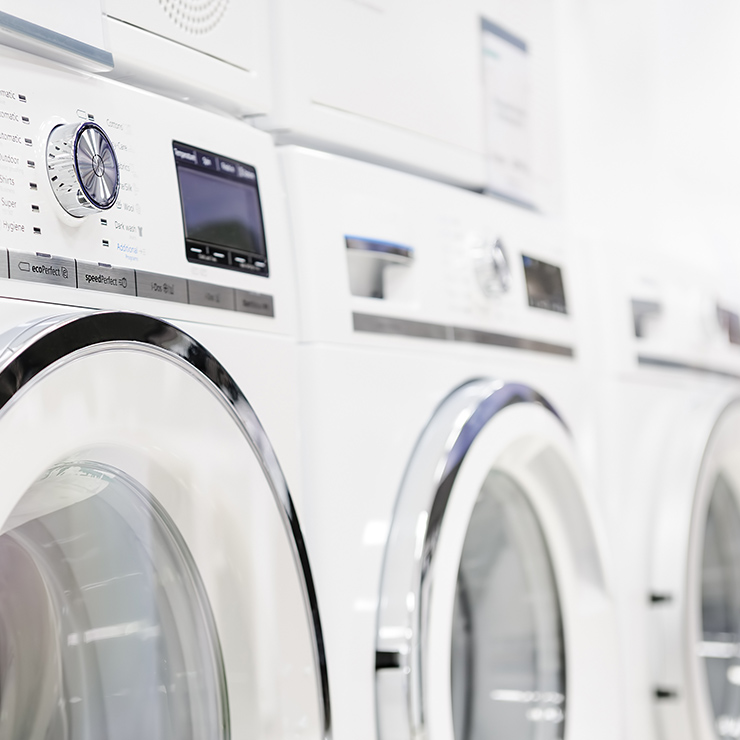 File di elettrodomestici bianchi, tra cui lavatrici e asciugatrici. I comandi sono visibili sul pannello frontale.