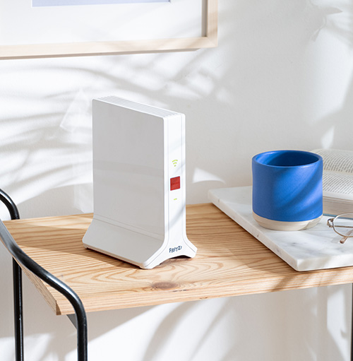 Su un ripiano di legno chiaro, un router bianco, una tazza blu e occhiali su un vassoio di marmo. Lo sfondo � bianco.
