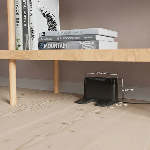 Scaffale in legno con libri. Sotto, un dispositivo nero con cavo. Il pavimento � in legno chiaro.