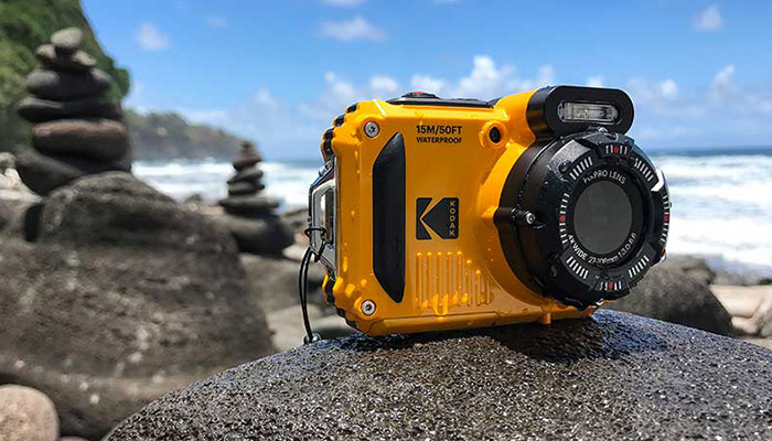 Una fotocamera gialla impermeabile Kodak è posizionata su una roccia, con l'oceano e le rocce impilate sullo sfondo.