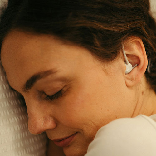 Donna addormentata su cuscino bianco con auricolari bianchi nell'orecchio destro.