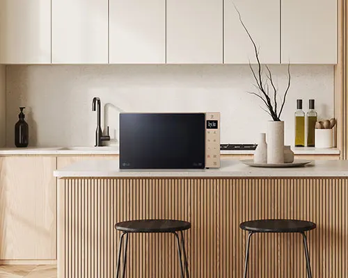 Cucina beige con forno a microonde nero, lavello, sgabelli e armadietti. Sul bancone ci sono accessori decorativi.