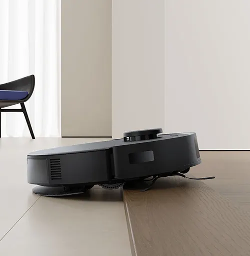 Aspirapolvere robot nero su pavimento in legno. Sullo sfondo, una sedia nera e pareti chiare.