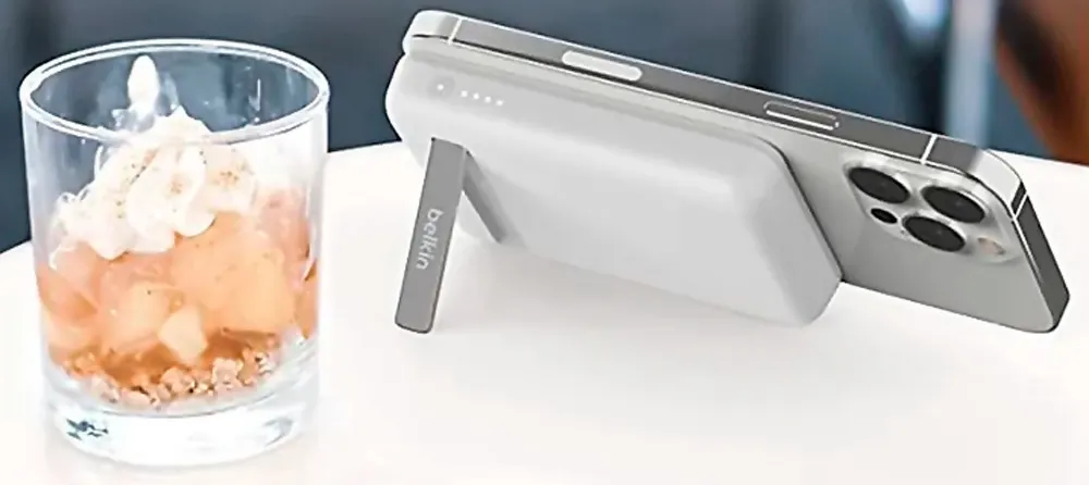 Su un tavolo bianco, un bicchiere con dessert e un telefono grigio appoggiato ad una batteria esterna Belkin.