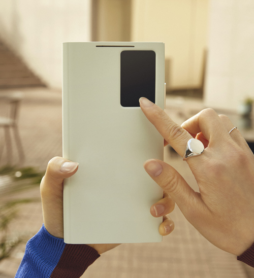 Un telefono bianco con un foro rettangolare nero viene tenuto in mano e toccato da un dito con un anello d'argento.
