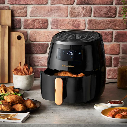 Friggitrice ad aria nera su un tavolo con cibo. Sullo sfondo, un muro di mattoni e taglieri di legno.