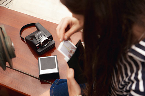 Donna che guarda una foto vicino a una macchina fotografica nera, un flash e una confezione quadrata su un tavolo.