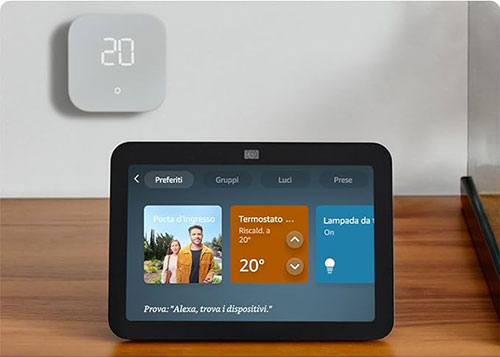 Tablet nero su tavolo di legno con display che mostra "Preferiti", "Termostato" e "Lampada". Un termostato quadrato bianco � montato sul muro.