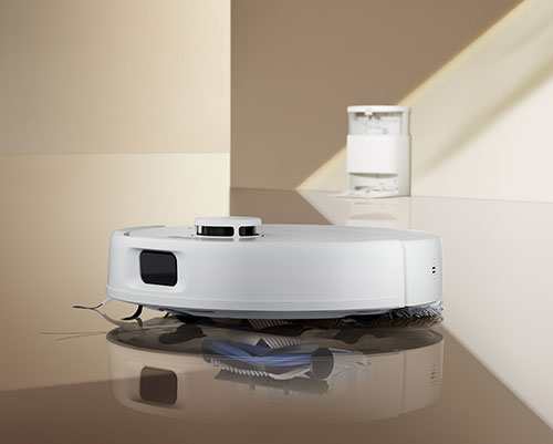 Aspirapolvere robot bianco su pavimento lucido, con contenitore bianco sullo sfondo e pareti beige.