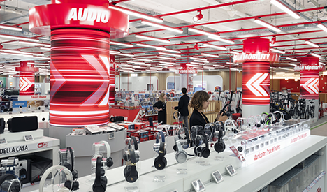Negozio di elettronica con scaffali di cuffie, illuminazione a neon e colonne rosse con scritte "Audio".
