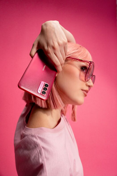 Donna con occhiali da sole, maglietta rosa e telefono. Lo sfondo è rosa.