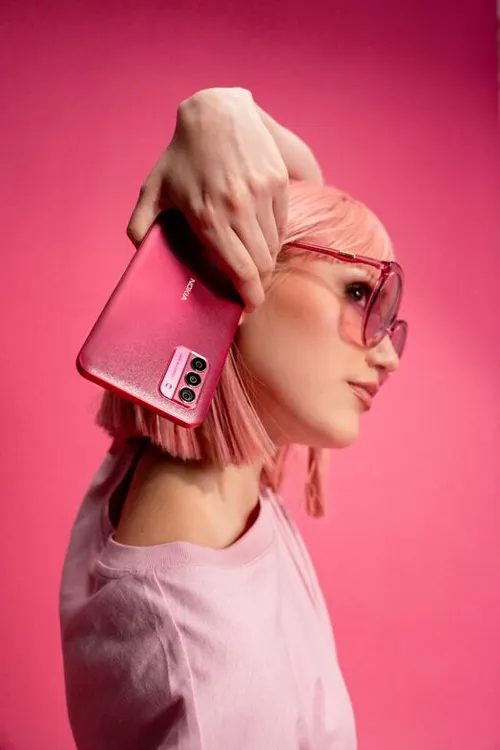 Donna con occhiali da sole, maglietta rosa e telefono. Lo sfondo è rosa.