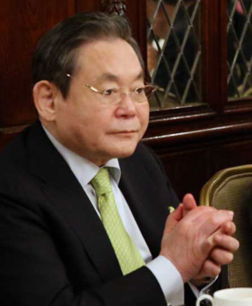 Uomo in giacca scura e cravatta verde, con occhiali, mani giunte. Sullo sfondo, finestra a losanghe e parte di una tazza bianca.