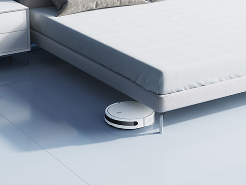 Un letto bianco con un comodino e un robot aspirapolvere sul pavimento bianco.