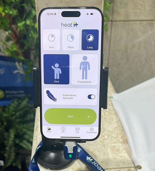 Telefono con app "heat it" aperta, montato su supporto. L'app ha opzioni per durata e utente. Pulsante verde "start".