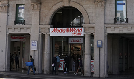 Facciata di un edificio con l'insegna "MediaWorld smart" sopra l'ingresso e persone all'interno.
