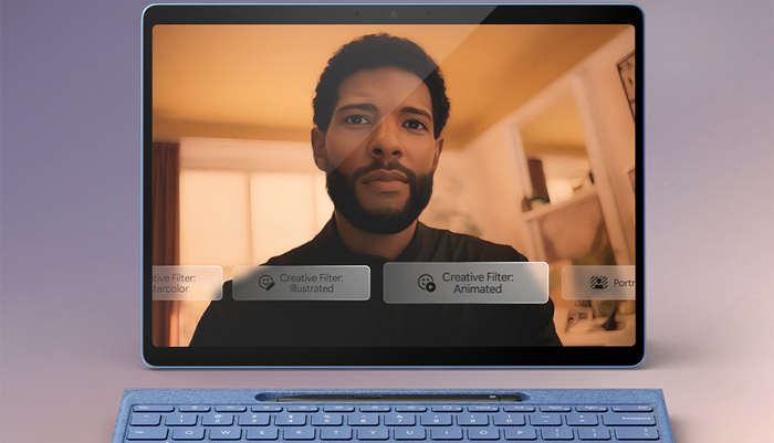 Tablet su tavolo con tastiera blu. Schermo mostra videochiamata di un uomo con barba e filtri creativi.