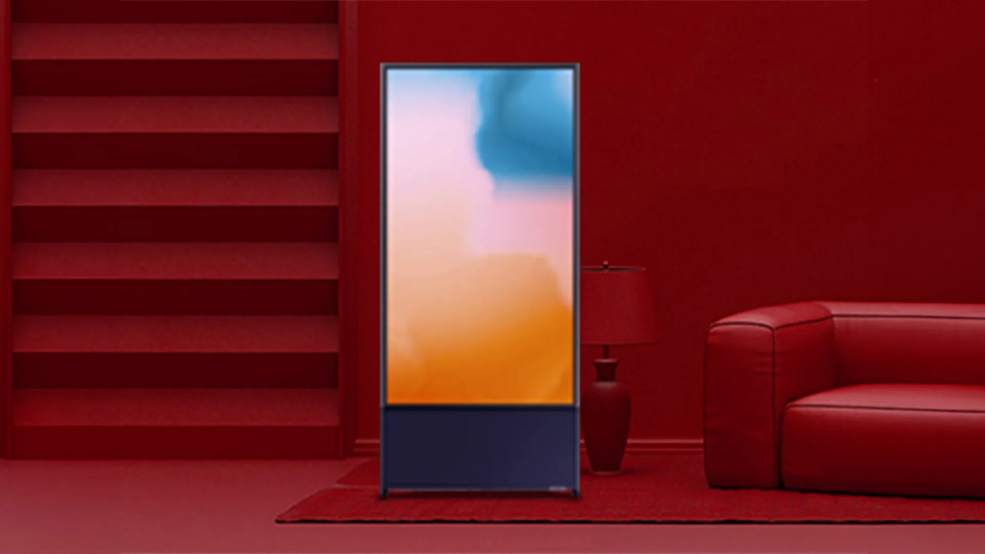 Interno rosso con divano, lampada e scala. Uno schermo verticale mostra sfumature blu, rosa e arancioni.