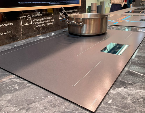 Pentola d'acciaio su piano cottura a induzione grigio con dettagli rettangolari. Sfondo marmorizzato.