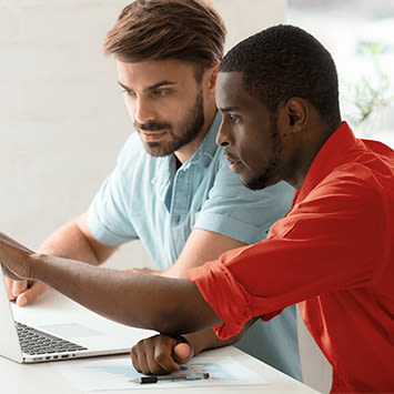 Due uomini guardano un laptop. Uno indossa una camicia azzurra, l'altro una rossa. Si trovano a un tavolo bianco.