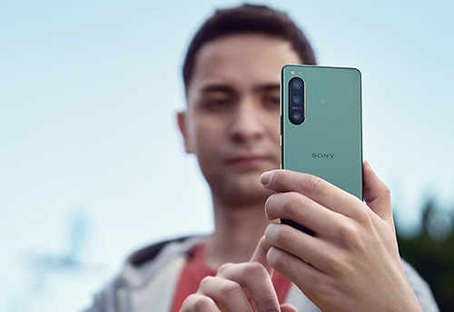 Uomo tiene in mano un telefono Sony verde. Il telefono ha tre fotocamere posteriori. Il cielo azzurro � sullo sfondo.