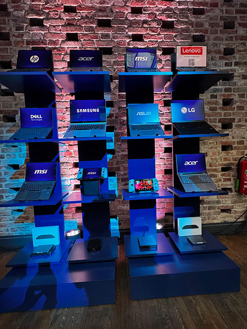 Esposizione di portatili di varie marche come MSI, Acer, Lenovo, Dell, Samsung e LG su scaffali blu a più livelli. Nintendo Switch.