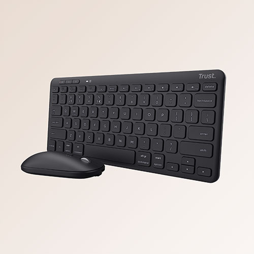 Tastiera nera e mouse su sfondo chiaro. La tastiera ha il marchio "Trust" in alto a destra.