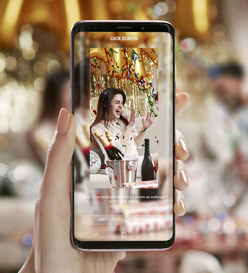 Mano che tiene un telefono con una donna che festeggia su uno sfondo festivo. Sul tavolo ci sono bottiglie di champagne in un secchiello.