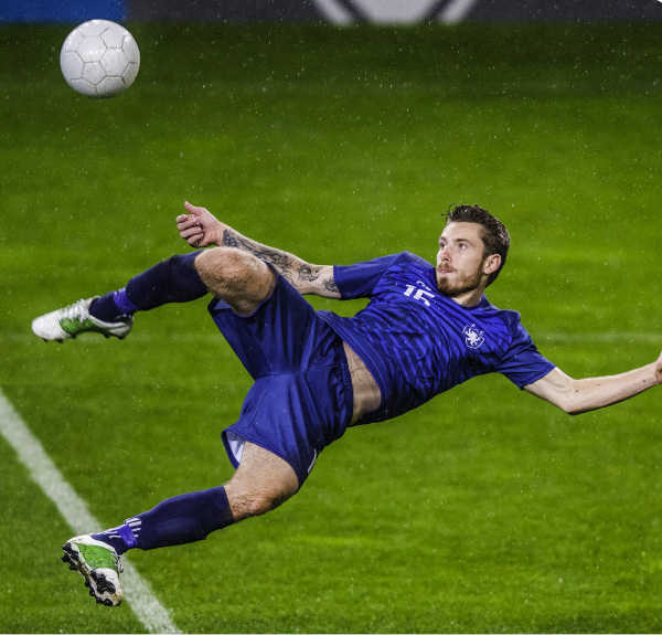 Un giocatore di calcio in blu calcia un pallone bianco su un campo verde. Il giocatore è in aria.
