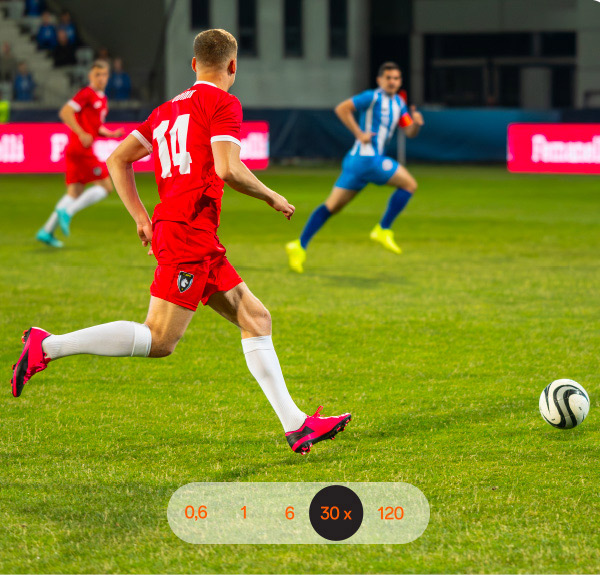 Un campo da calcio verde con giocatori in rosso e blu che inseguono un pallone bianco e nero. Uno indossa la maglia numero 14.