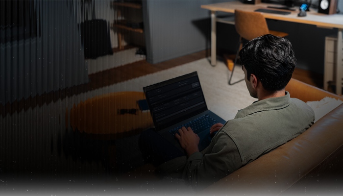 ragazzp girato di schiena e' seduto sul divano e ha un portatile sulle gambe