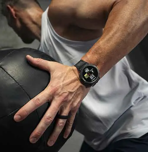 Uomo in canottiera bianca che tiene una palla nera. Indossa un orologio digitale al polso sinistro e un anello nero.