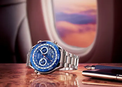 Orologio blu su tavolo lucido vicino a penna stilografica. Finestrino aereo con cielo al tramonto sullo sfondo.