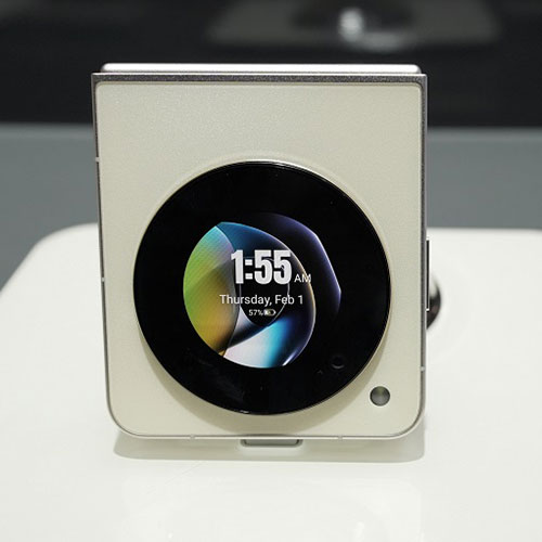 Orologio digitale quadrato beige con display nero rotondo che mostra l'ora, la data e un'immagine astratta.