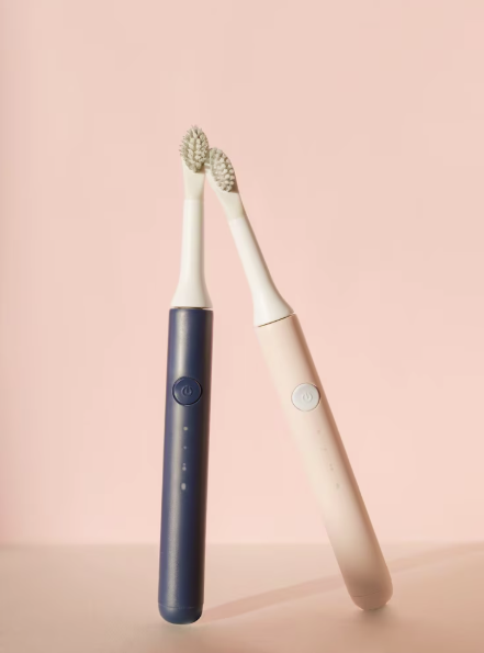 Due spazzolini elettrici, uno blu e uno rosa, appoggiati su sfondo rosa.