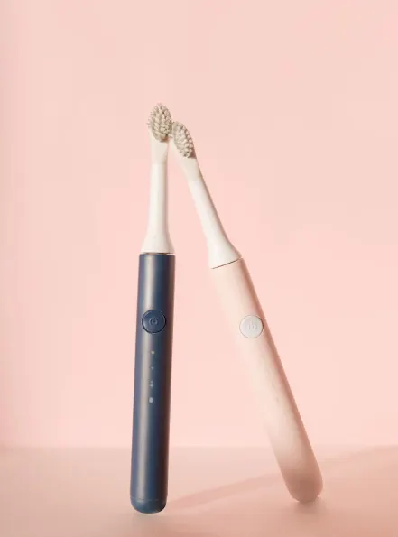 Due spazzolini elettrici, uno blu e uno rosa, appoggiati su sfondo rosa.