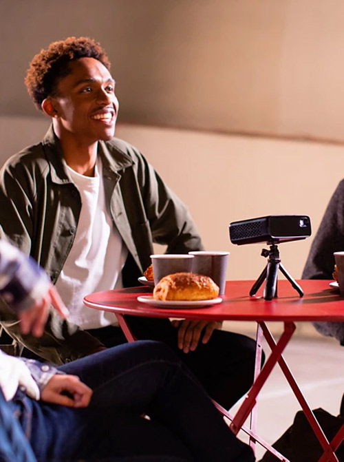 Uomini seduti a un tavolo rosso con un proiettore, croissant e caffè.