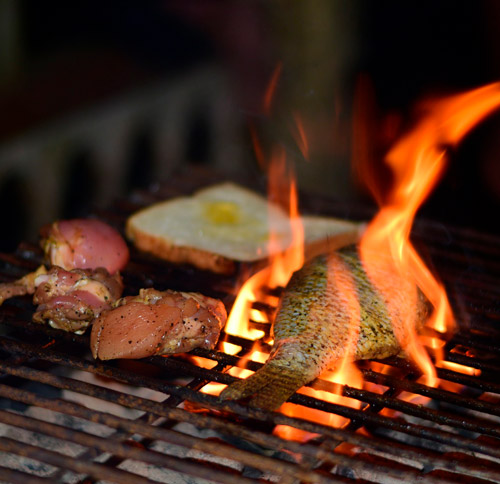 Griglia con fiamme. Si vedono carne, pesce e uovo cotto. Il fuoco � acceso sotto la griglia.