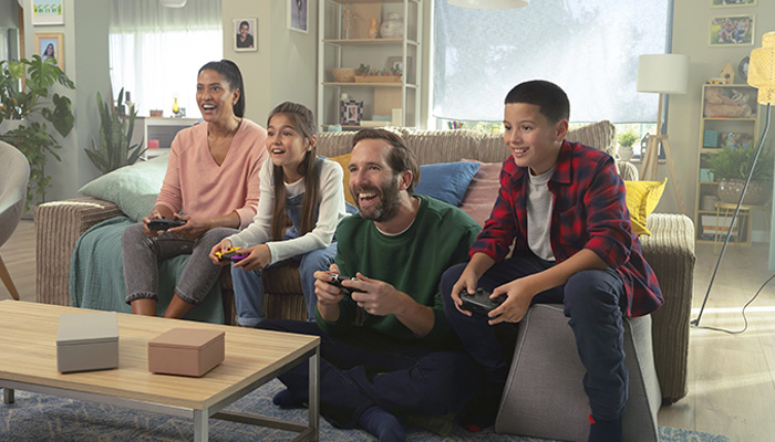 Quattro persone sedute su un divano giocano con dei controller. Un tavolino basso è davanti al divano.