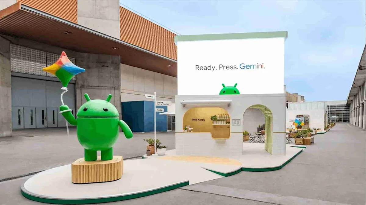 Statua verde Android con palloncino colorato vicino a chiosco informativo con scritta "Ready. Press. Gemini.".